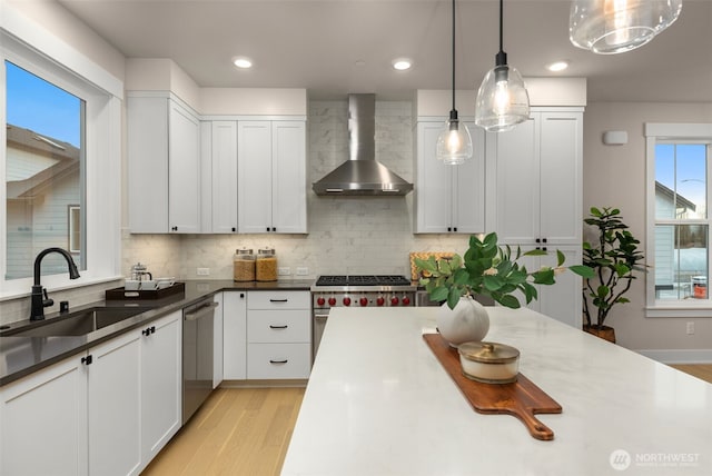 kitchen with light wood-style flooring, stainless steel appliances, a sink, white cabinetry, and wall chimney exhaust hood