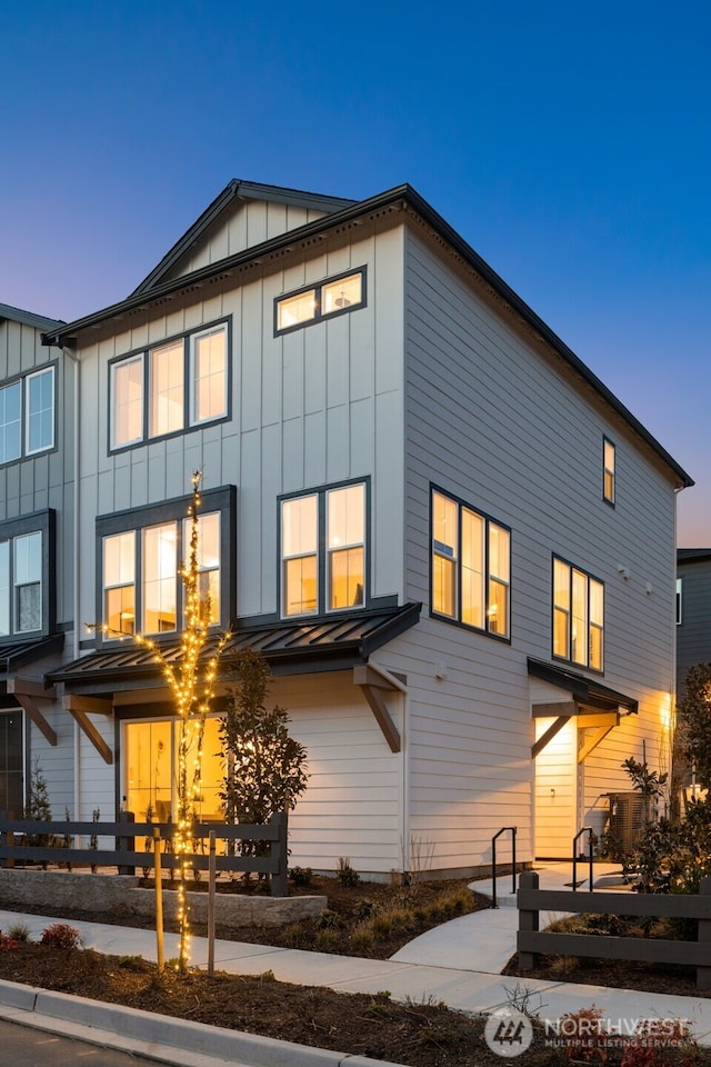 back of house at dusk featuring a standing seam roof, metal roof, board and batten siding, and fence