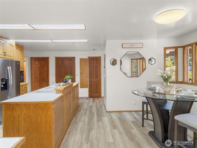 kitchen with a center island, baseboards, light countertops, light wood-style flooring, and stainless steel fridge