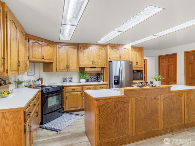 kitchen with light wood-type flooring, a kitchen island, black appliances, and light countertops