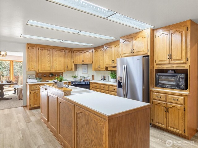 kitchen with light wood finished floors, a kitchen island, stainless steel fridge with ice dispenser, a sink, and black microwave