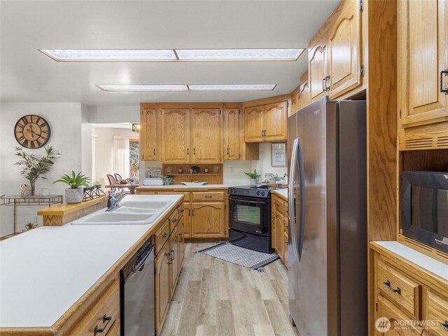 kitchen with black appliances, light countertops, light wood-style floors, and a sink