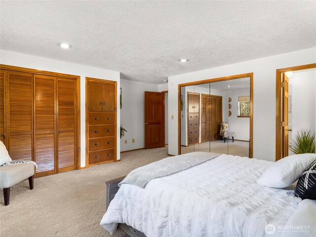 bedroom featuring light carpet, recessed lighting, two closets, and a textured ceiling