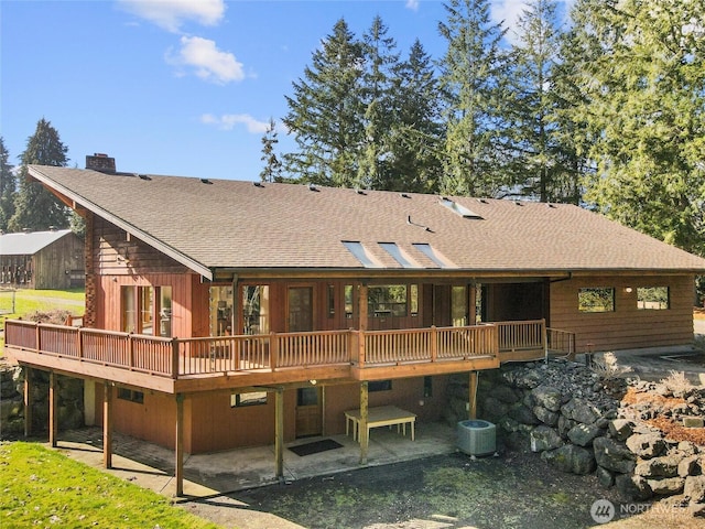 rear view of house featuring a wooden deck, a patio, a chimney, and a shingled roof