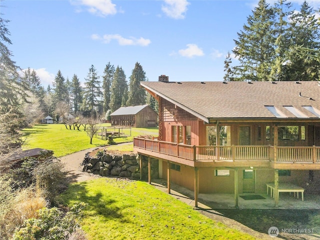 rear view of property with a shingled roof, a chimney, a deck, a yard, and a patio area