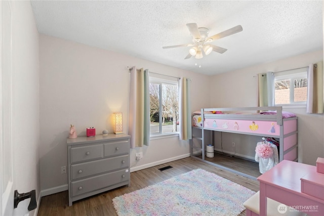 bedroom featuring a textured ceiling, multiple windows, visible vents, and wood finished floors