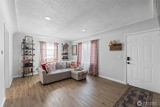 living room with a textured ceiling, baseboards, and wood finished floors