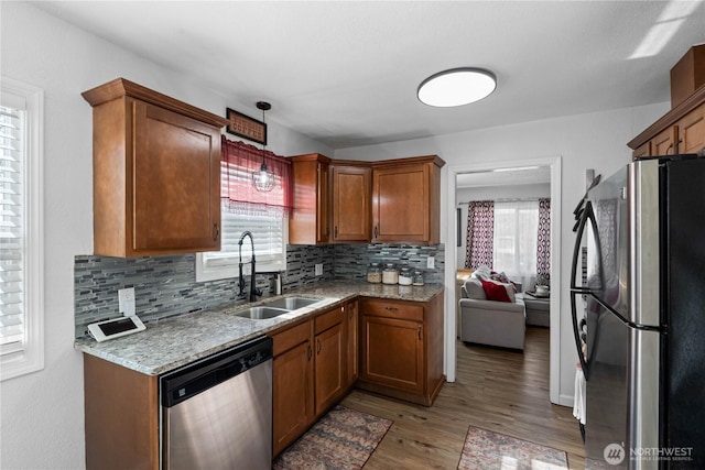 kitchen featuring light wood finished floors, dishwasher, brown cabinets, freestanding refrigerator, and a sink