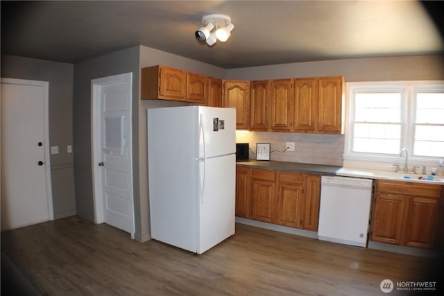 kitchen with brown cabinets, white appliances, wood finished floors, and a sink