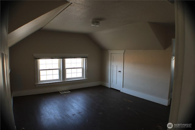 bonus room with visible vents, dark wood-type flooring, a textured ceiling, baseboards, and lofted ceiling