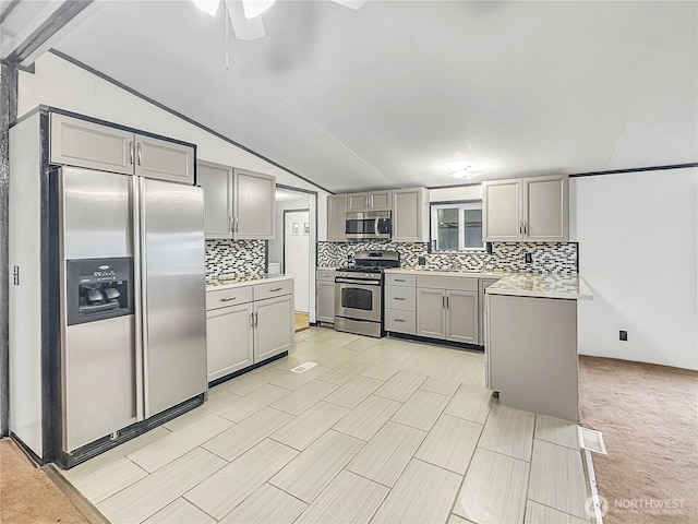 kitchen featuring backsplash, gray cabinetry, light countertops, vaulted ceiling, and appliances with stainless steel finishes