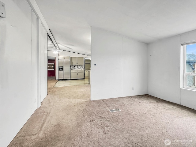 unfurnished room featuring visible vents, light carpet, and vaulted ceiling