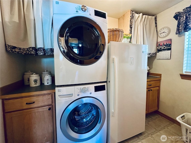 washroom featuring cabinet space, stacked washer and clothes dryer, and baseboards