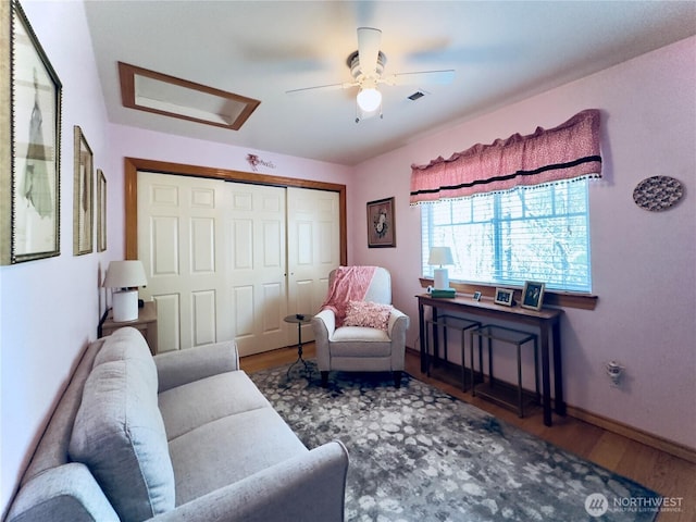 living area featuring ceiling fan, attic access, baseboards, and wood finished floors