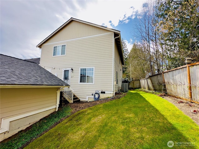 rear view of property with a fenced backyard, central air condition unit, a yard, and roof with shingles