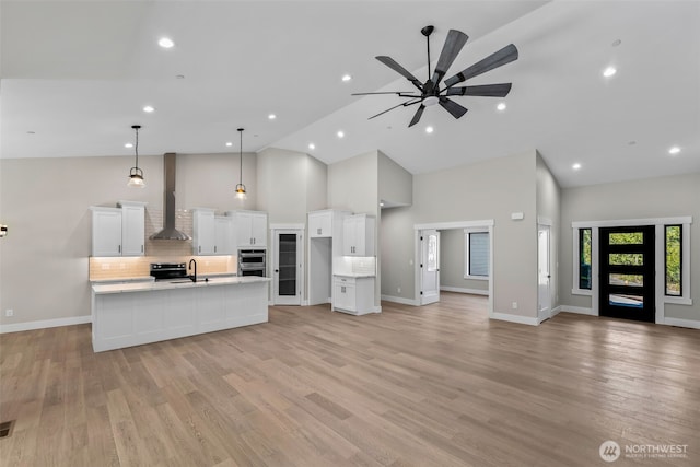 kitchen with a sink, backsplash, open floor plan, white cabinetry, and wall chimney exhaust hood