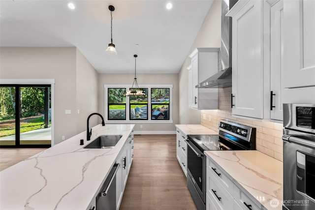 kitchen featuring a sink, appliances with stainless steel finishes, white cabinetry, wall chimney range hood, and backsplash