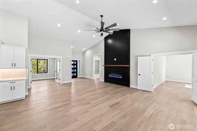 unfurnished living room with high vaulted ceiling, baseboards, light wood-style floors, and a fireplace