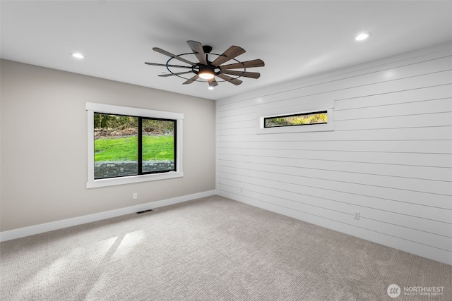 carpeted spare room with visible vents, a ceiling fan, recessed lighting, wooden walls, and baseboards