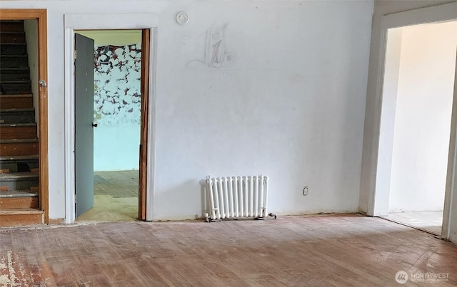 empty room featuring radiator, stairway, and wood finished floors