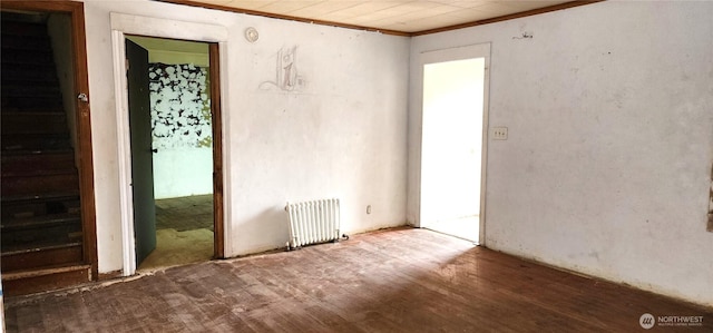 empty room featuring ornamental molding, radiator, and wood finished floors