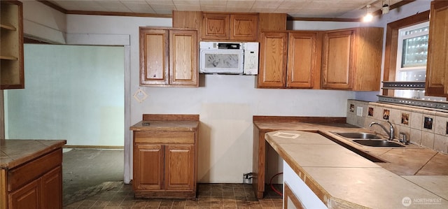 kitchen with white microwave, tile counters, brown cabinetry, and a sink