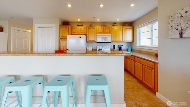 kitchen with recessed lighting, white appliances, a breakfast bar area, light tile patterned flooring, and light stone countertops