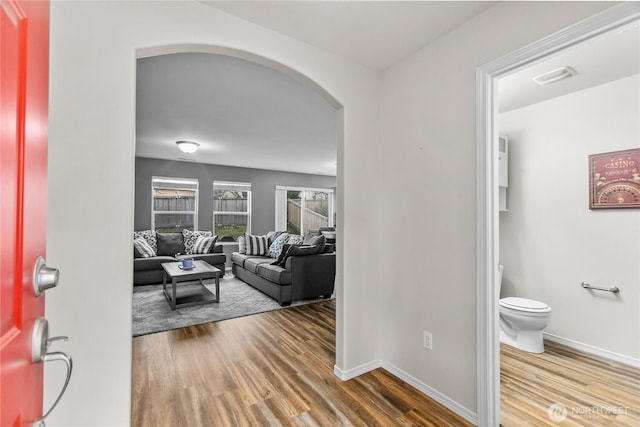 foyer entrance with baseboards, arched walkways, and wood finished floors