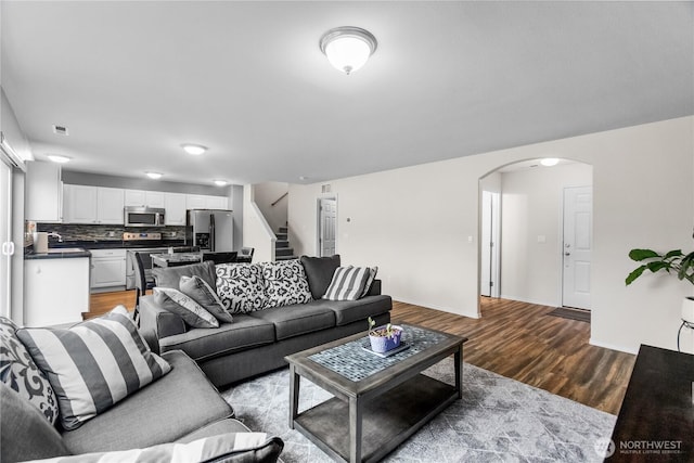 living area featuring arched walkways, wood finished floors, visible vents, baseboards, and stairway