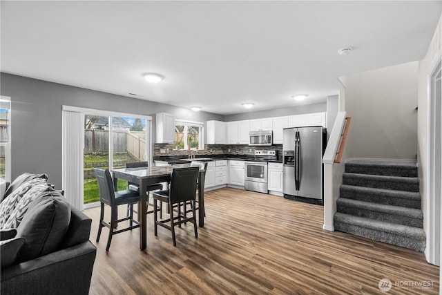 kitchen featuring stainless steel appliances, wood finished floors, white cabinetry, tasteful backsplash, and dark countertops