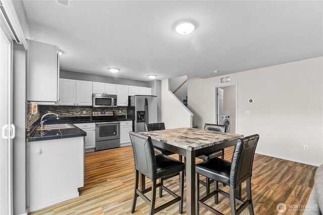 kitchen with stainless steel appliances, light wood-style flooring, white cabinets, a sink, and washer / dryer