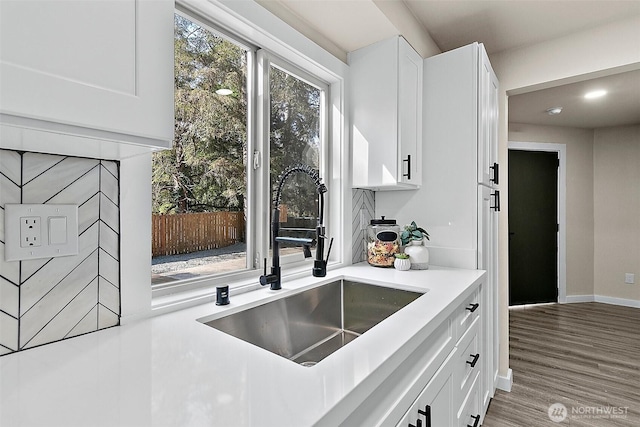 kitchen with baseboards, wood finished floors, light countertops, white cabinetry, and a sink