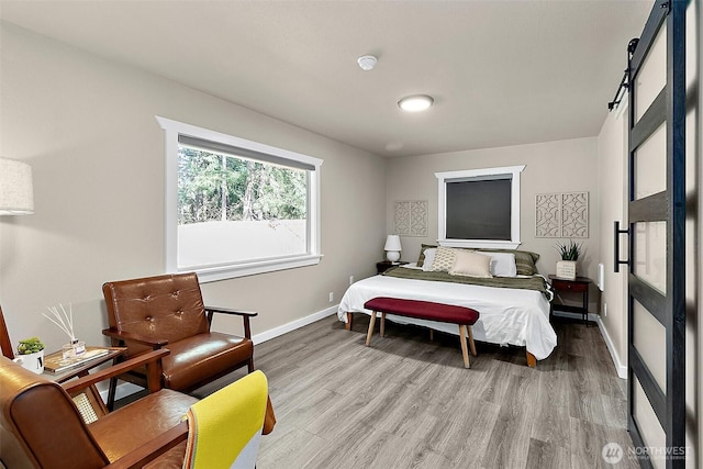 bedroom with a barn door, baseboards, and wood finished floors