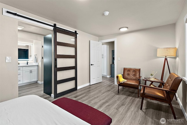 bedroom featuring ensuite bath, light wood-style flooring, baseboards, and a barn door