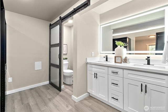 bathroom featuring double vanity, a sink, toilet, and wood finished floors