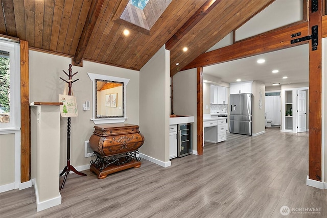 interior space featuring stainless steel refrigerator with ice dispenser, tasteful backsplash, lofted ceiling with skylight, white cabinets, and light wood-type flooring