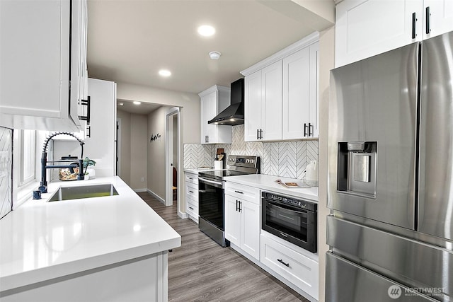 kitchen with stainless steel appliances, tasteful backsplash, light countertops, a sink, and wall chimney range hood