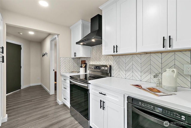 kitchen featuring light wood finished floors, light countertops, electric range, white cabinets, and wall chimney exhaust hood