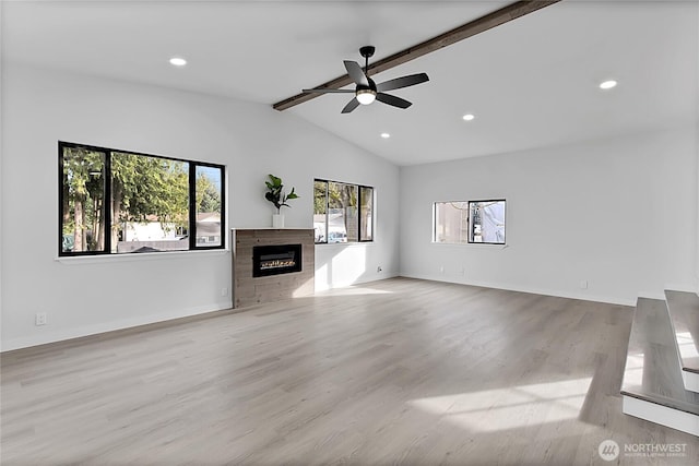 unfurnished living room featuring lofted ceiling with beams, wood finished floors, a glass covered fireplace, and baseboards