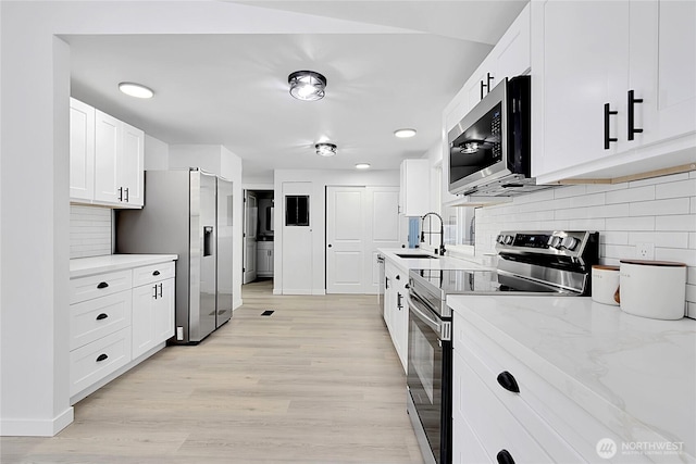 kitchen featuring stainless steel appliances, a sink, white cabinets, and light wood-style floors