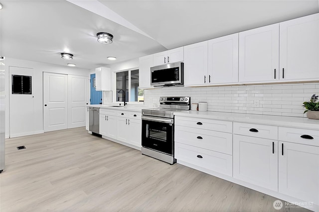 kitchen featuring stainless steel appliances, light countertops, decorative backsplash, a sink, and light wood-type flooring