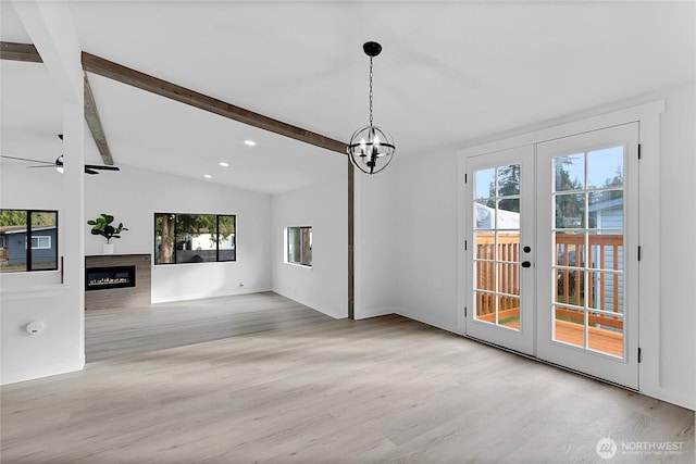 unfurnished living room with french doors, lofted ceiling with beams, a glass covered fireplace, wood finished floors, and ceiling fan with notable chandelier