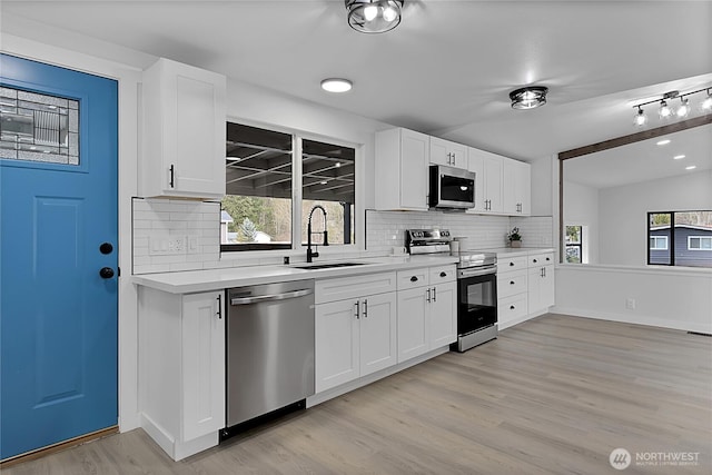 kitchen with tasteful backsplash, stainless steel appliances, light countertops, light wood-type flooring, and a sink