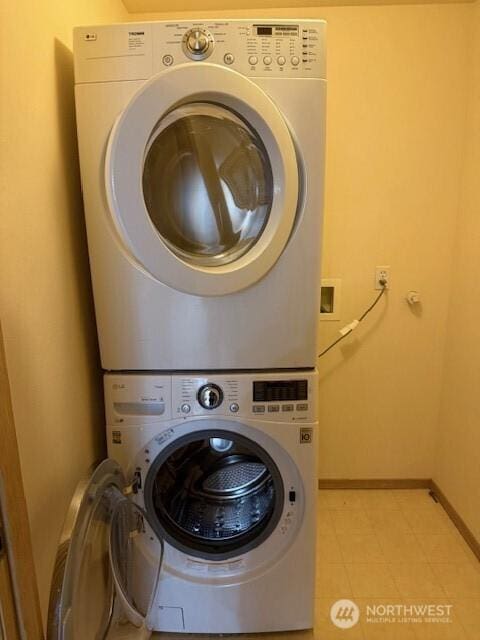 clothes washing area featuring light tile patterned flooring, laundry area, baseboards, and stacked washer and dryer