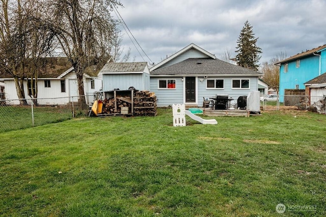 back of house featuring a yard, a shingled roof, an outdoor structure, and a fenced backyard