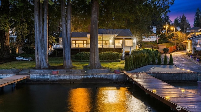 back of house at dusk with stairway, a yard, and a deck with water view