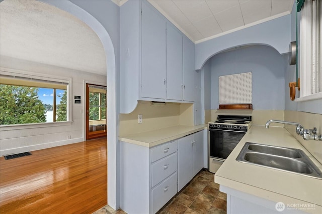 kitchen featuring visible vents, light countertops, electric stove, arched walkways, and a sink