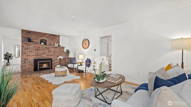 living area featuring a brick fireplace, wood finished floors, baseboards, and a textured ceiling