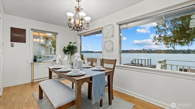 dining area featuring wood finished floors, a textured ceiling, a chandelier, and a water view