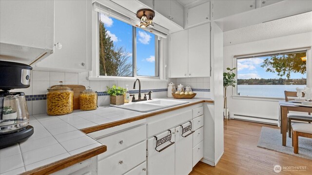 kitchen featuring a wealth of natural light, baseboard heating, tile countertops, and a sink